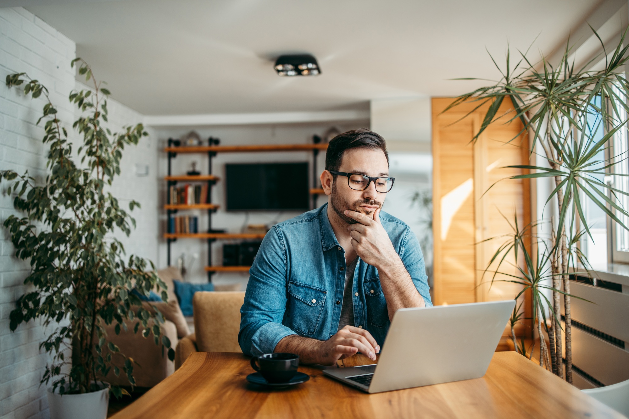 Portrait of a casual businessman thinking while looking at laptop screen, keeping hand on chin.