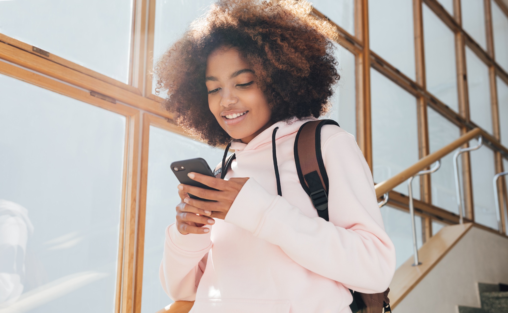 Smiling girl looking at her smartphone while going down on stairs in school